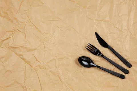 Reusable recyclable black fork, spoon, knife made from corn starch on brown c Stock Photos