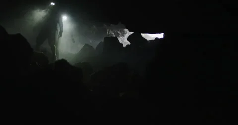 Reveal two explorers passing through smoke in a cave Stock Footage 64682717