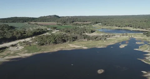 Reverse aerial view of lake and green camping farm in australia 스톡 동영상 100615385