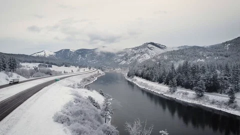Reverse dolly shot over river and train tracks surrounded by snow and evergre Stock Footage 125491240