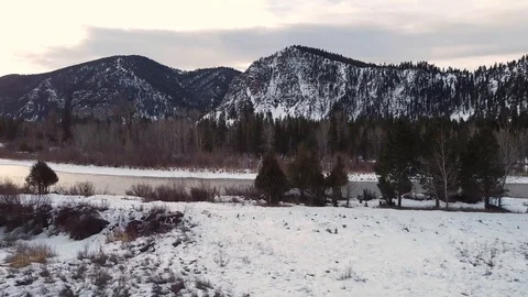 Reverse overhead dolly shot above snow covered field away from trees and rive Stock Footage 125401616