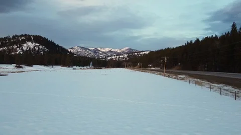 Reverse overhead dolly shot along empty highway over snow covered field away Stock Footage 125384482