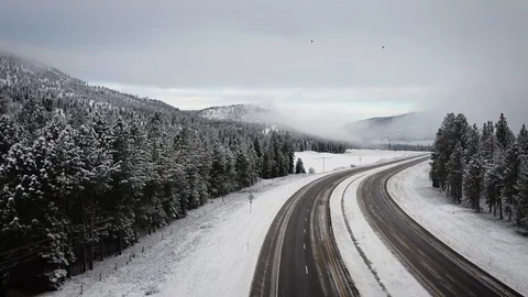 Reverse overhead dolly shot of empty highway surrounded by snow and trees wit Stock Footage 125491088