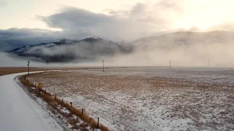 Reverse overhead shot over snow covered pasture with fog shrouded mountain ra Stock Footage 124713952