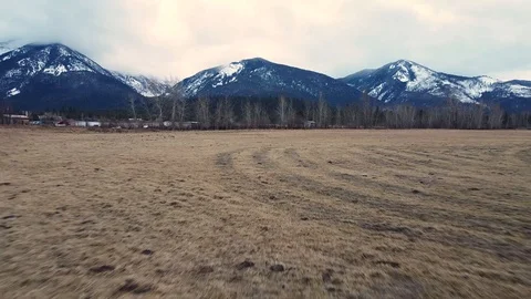 Reverse shot tracking down an empty pasture towards a tree line and snow capp Stock Footage 125050625