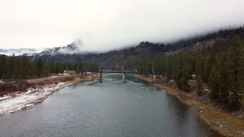 Reverse tracking shot over wide river toward train bridge away from mountain Stock Footage 125054182