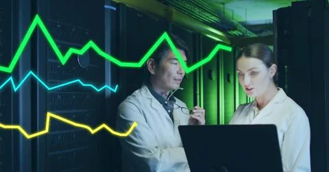 Reviewing data on laptop, engineers in lab coats checking servers in data Stock Photos