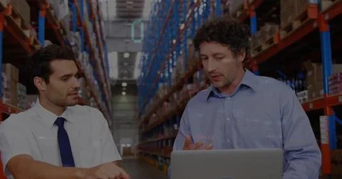 Reviewing stock data two men in business attire typing on laptop in warehouse Stock Photos