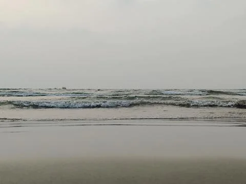 Rhythmic ocean waves rolling onto a flat beach under a hazy sky Stock Photos