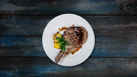 Rib-eye steak with corn rotating on a white plate. Top view on a wooden Stock Footage 102671619