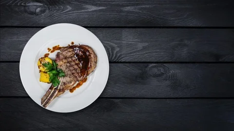 Rib-eye steak with corn rotating on a white plate. Top view on black wooden Stock Footage 102673443