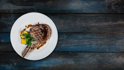 Rib-eye steak with corn rotating on a white plate. Top view on a wooden Stock Footage 102674474