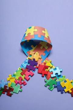 Ribbon with multi-colored puzzle pieces on a light background. World autism.. Stock Photos