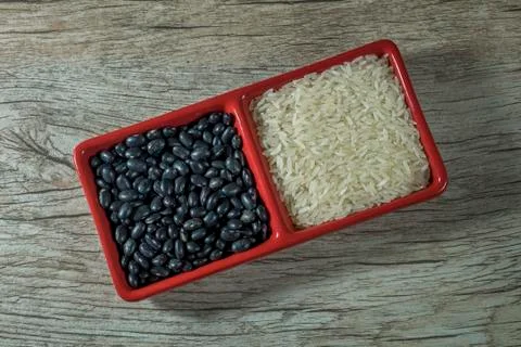 Rice and black beans crude in red container on wooden background Stock Photos