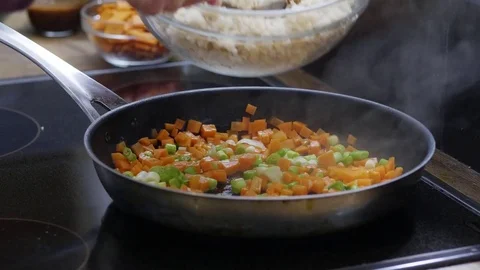 Rice being added into a frying pan with sauteed carrots and spring onions Stock Footage 84493981