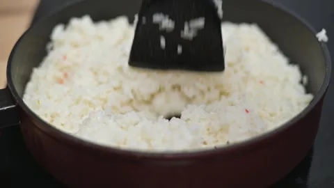 Rice is being stirred in a black pan on a stovetop. The activity showcases a Stock Footage 338298656