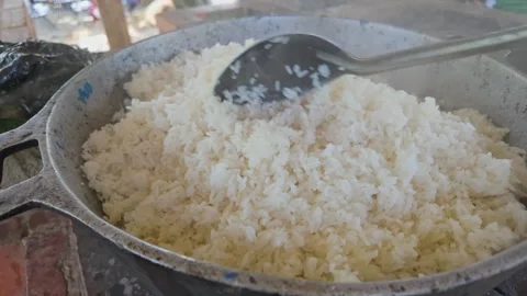 Rice cooked with firewood in an iron container, stirred with a large Stock Footage 280162915