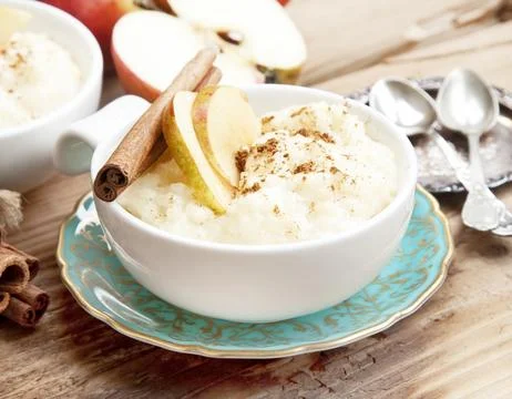 Rice Pudding with Apple Slices and Cinnamon Spice Sticks on Wooden Background Stock Photos