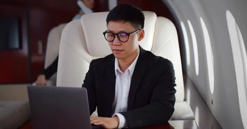Rich asian businessman flying first class and working on plane with laptop Stock Photos