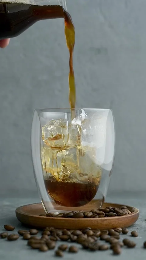 Rich cold brew cascades over crystal ice cubes in a clear glass, promising chill Stock Footage 305931097