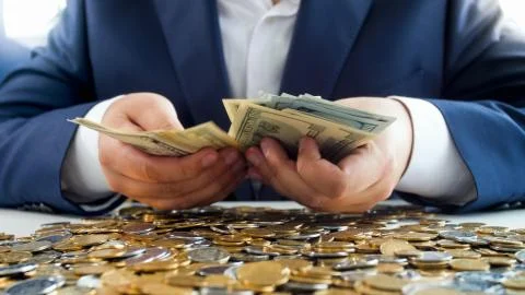 Rich man hands holding stack of money on heap of coins. Concept of financial Stock Photos