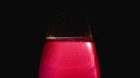 A rich ruby red beverage in glass flask illuminated against dark background Stock Footage 320418960