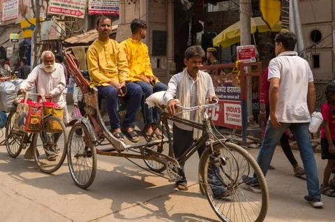 Rickshaw puller transporting two men on a busy main street in Varanasi, India. Stock Photos