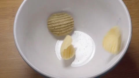 Ridged Potato Chips Falling Into White Bowl on Wooden Table During Snack Stock Footage 343971197