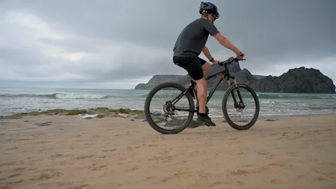 Riding mountain bike on the beach while the waves roll in Stock Footage 114502269