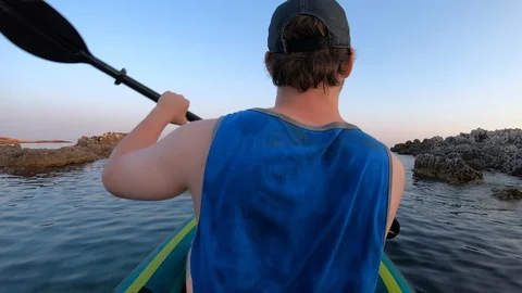 Right behind shot: Young man paddling his kayak carefully along the rugged coast Stock Footage 112185910