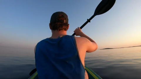 Right behind shot: Young man paddling his kayak across the calm sea as the sun Stock Footage 112186412