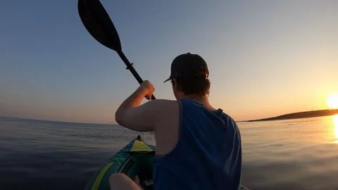 Right behind shot: Young man paddling his kayak across the calm sea at sunset Stock Footage 112186424