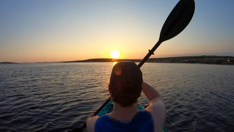 Right behind shot: Young man paddling in his sea kayak into the sunset Stock Footage 112187906