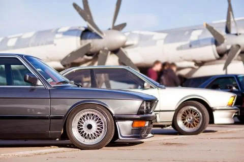 Right front side of two old european sport cars with plane on background Stock Photos