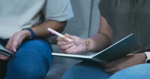 Right hand is pausing over notebook on sofa, reaching, passing pen, left is Stock Footage 344655128