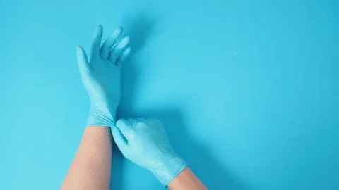 Right hand is pulling blue latex gloves of left hand on blue background. Stock Photos