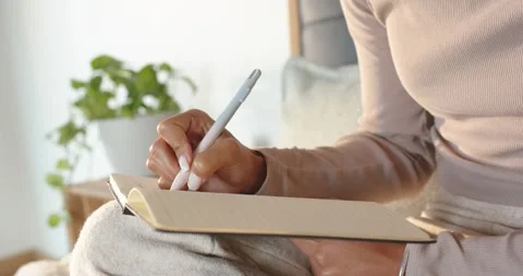 Right hand is writing in lined notebook on couch as pen is touching paper, Stock Footage 347801699