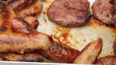 Right to left pan across a joint of beef, sausages and burgers at a BBQ 库存影片 80436747