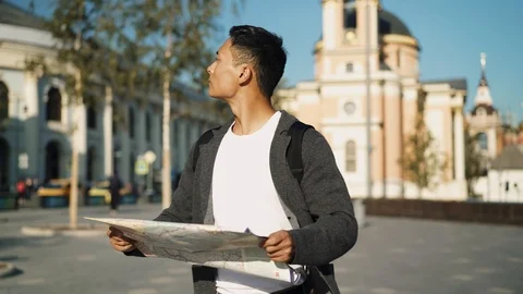 Right to left pan real time portrait shot of a young Asian man looking at a map 스톡 동영상 124095854