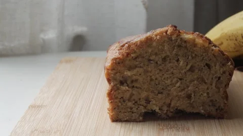 Right pan view of banana bread cut in half on a wooden board with a bananas in 스톡 동영상 296573682