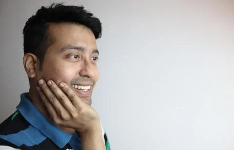 Right side of a cute face of an asian man with hand on chin smiling, feeling Stock Photos