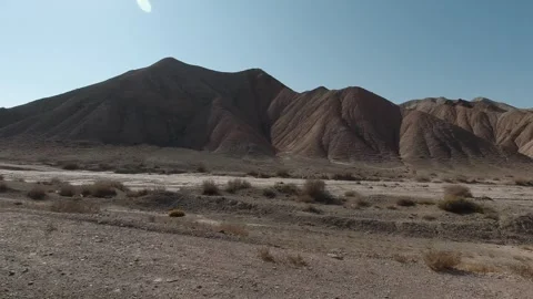 Right-side tracking view of eroded desert hills and dry riverbed in harsh sun Stock Footage 319794775