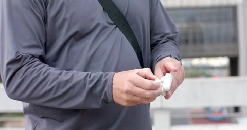 Right thumb is flipping open wireless earbud case, man removing earbud for Stock Footage 340256892