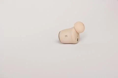 Right wireless earbud close-up on a light background. Stock Photos