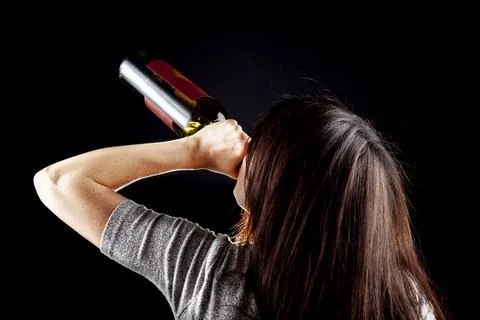 Rim light from behind image of a young caucasian woman drinking wine from bot Stock Photos
