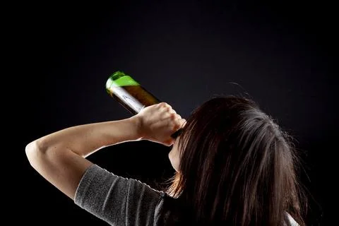 Rim light from behind image of a young caucasian woman drinking beer from bot Stock Photos
