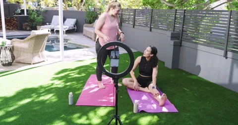 Ring light activating diverse female friends guiding hamstring stretch on mats Stock Footage 314027300