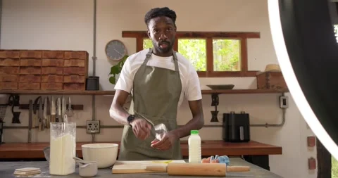 Ring light filming African man in apron cracking eggs adding milk whisking in Stock Footage 341944901