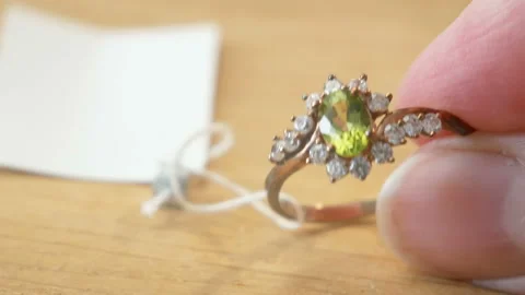 Ring with peridot stone and diamonds in hands on wooden background Stock Footage 156740448