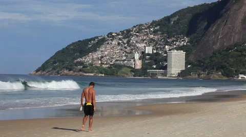 Rio de Janeiro: Man Walks Down Beach with a Slum in the Background Stock Footage 45332062